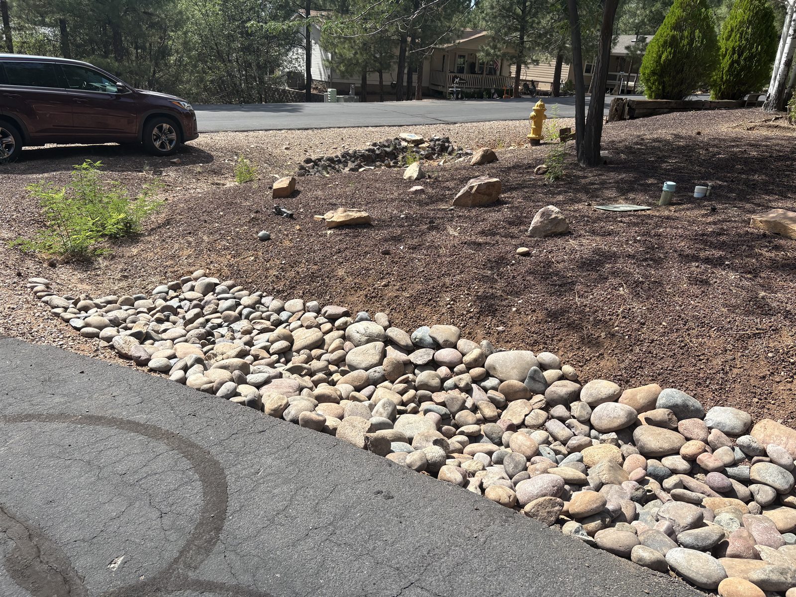 Rounded river stones along an asphalt driveway beside reddish gravel and landscape boulders