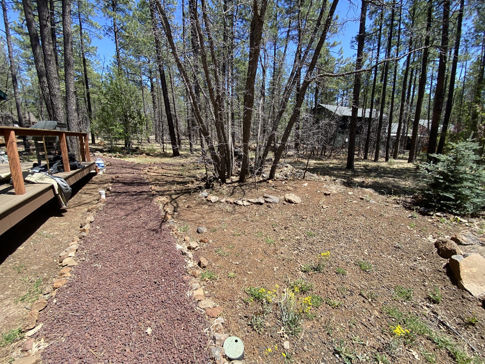 Reddish gravel path edged with stones beside a wooden deck and a cleaned wooded yard